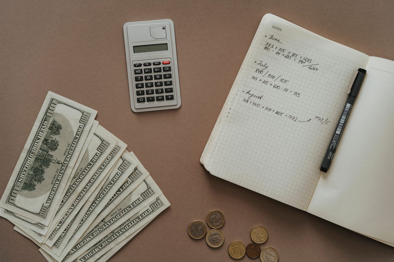 A calculator, a fan of banknotes and an open notebook arranged on a desk