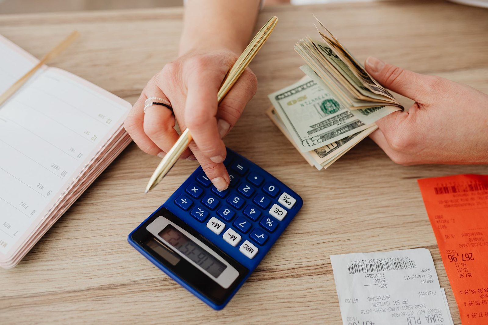 Hands counting banknotes over an open notebook with a calculator on the desk