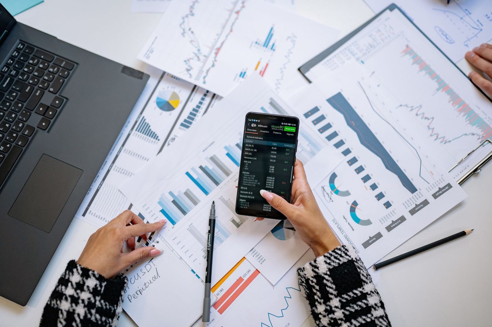 Hands working over printed charts with a phone displaying data