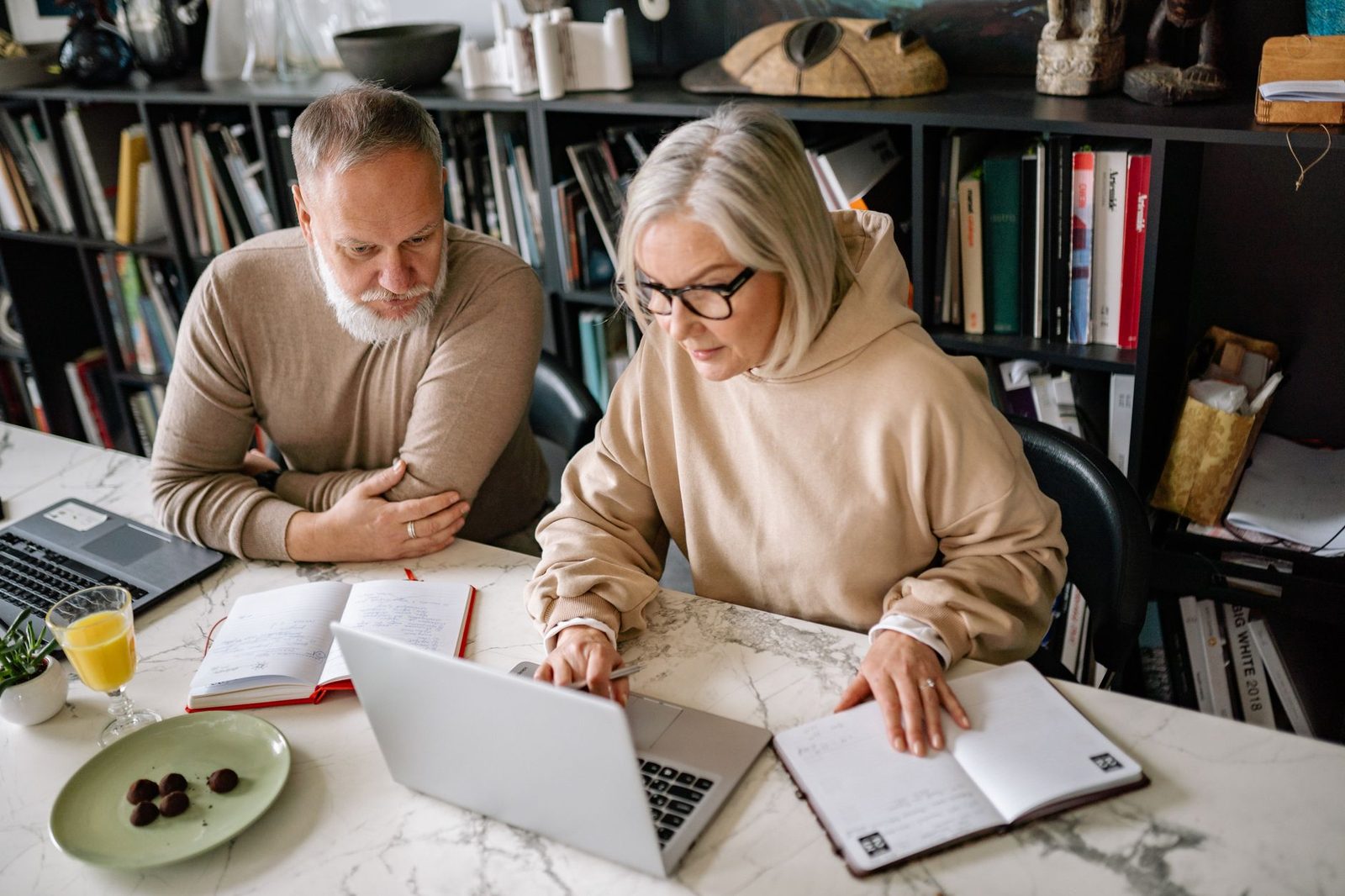 A couple working at a shared desk with two laptops and printed pages