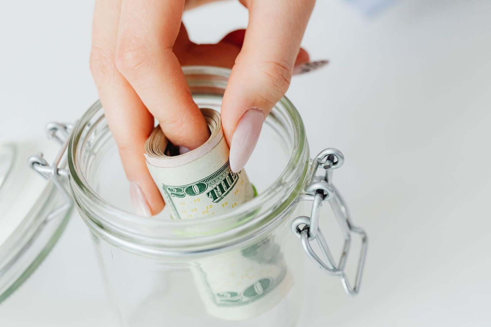 A hand placing a rolled banknote into a glass jar