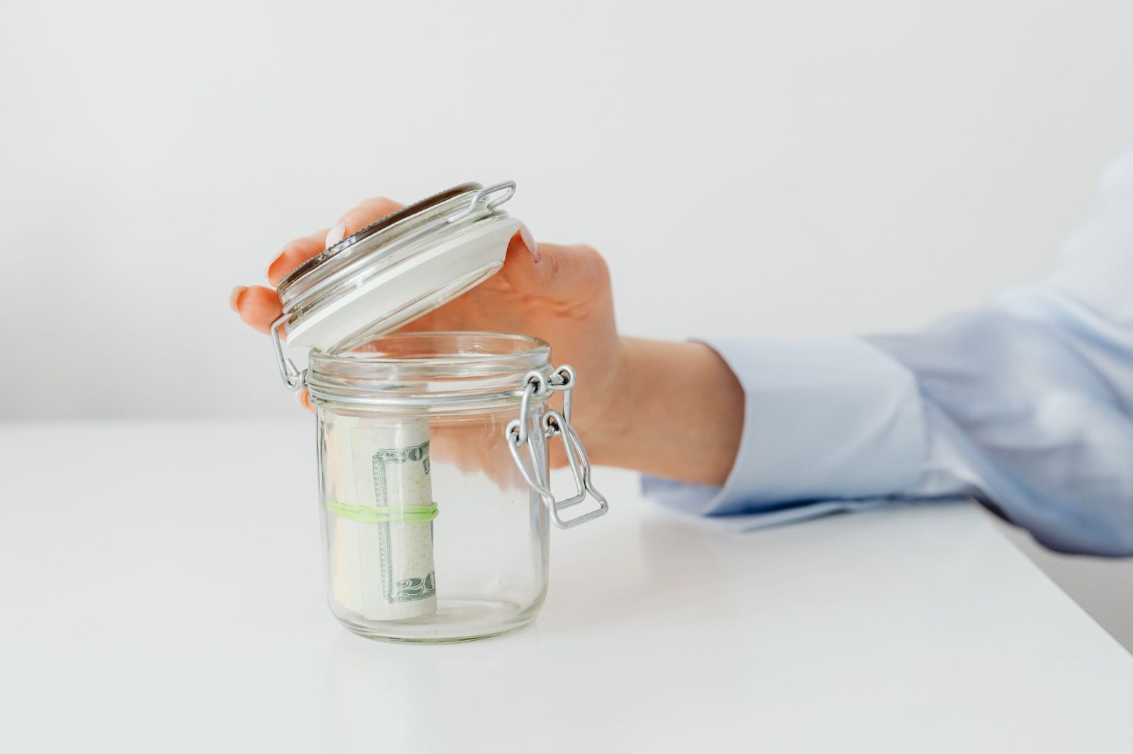 A glass storage jar holding folded banknotes on a light desk