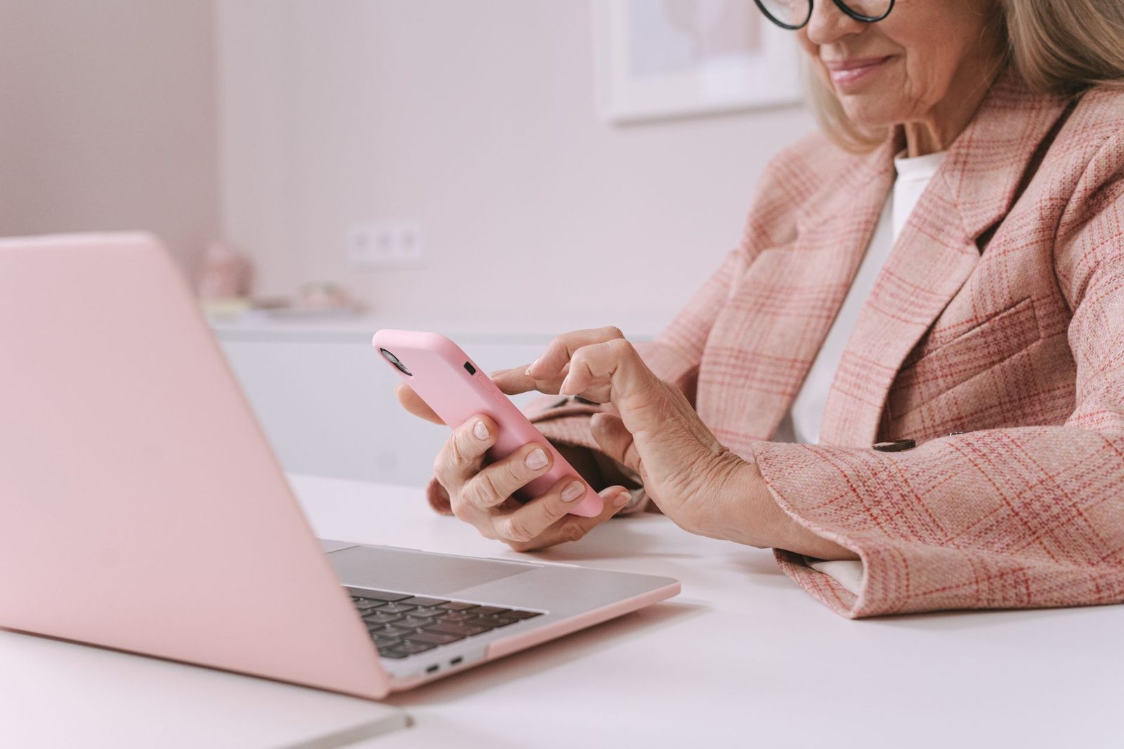 An older woman using a laptop while holding a phone