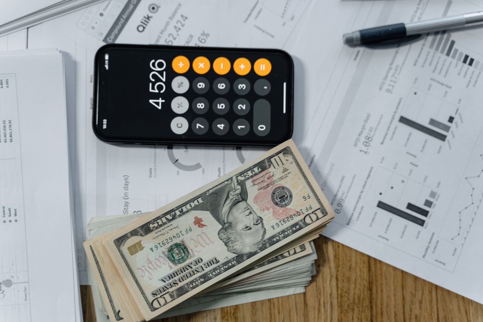 A calculator resting on printed documents beside a banknote