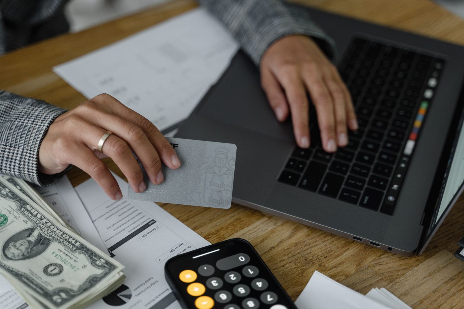 Hands at a laptop keyboard with banknotes and a calculator on the desk