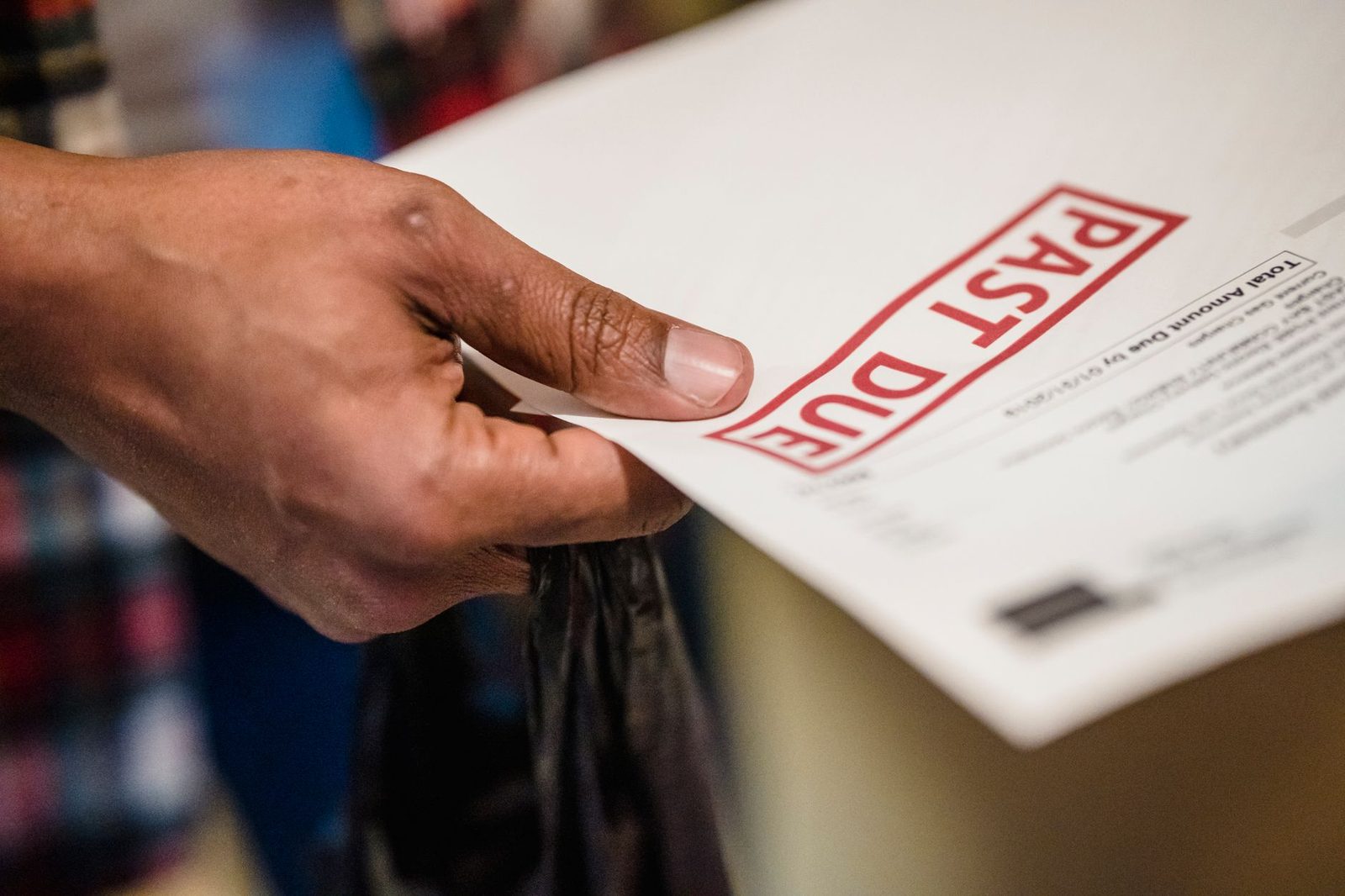 A hand holding an envelope stamped past due in red ink