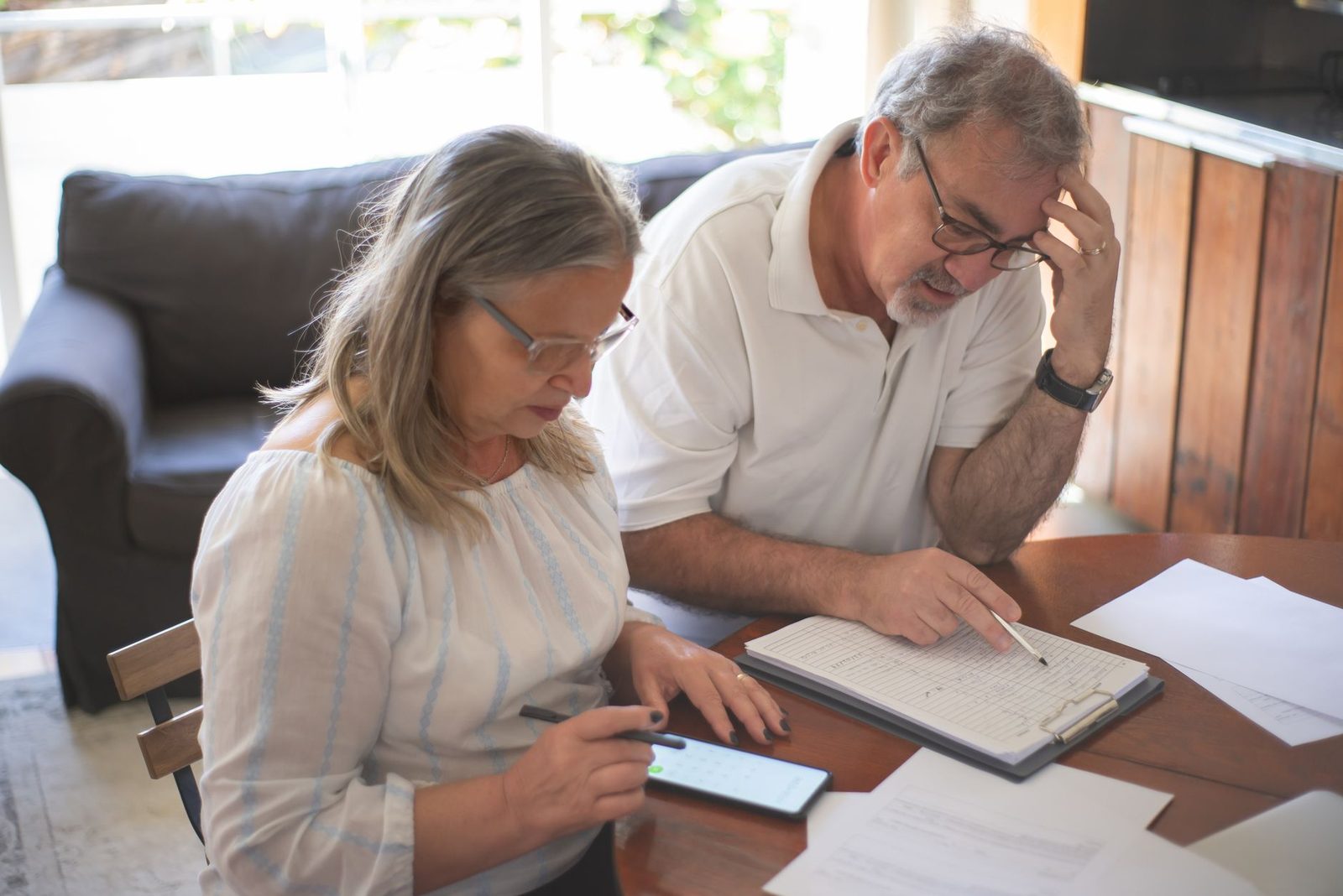 An older couple reviewing printed documents at a table, one holding a phone