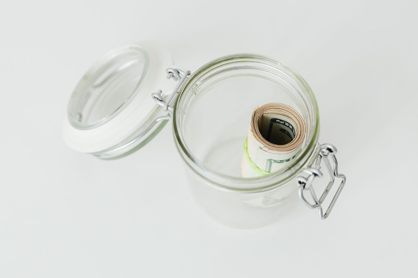 A glass jar containing rolled banknotes on a plain surface