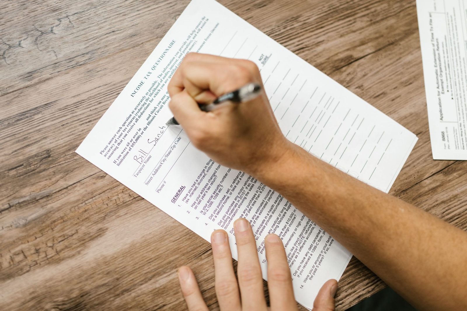 A hand filling in a printed tax form with a pen