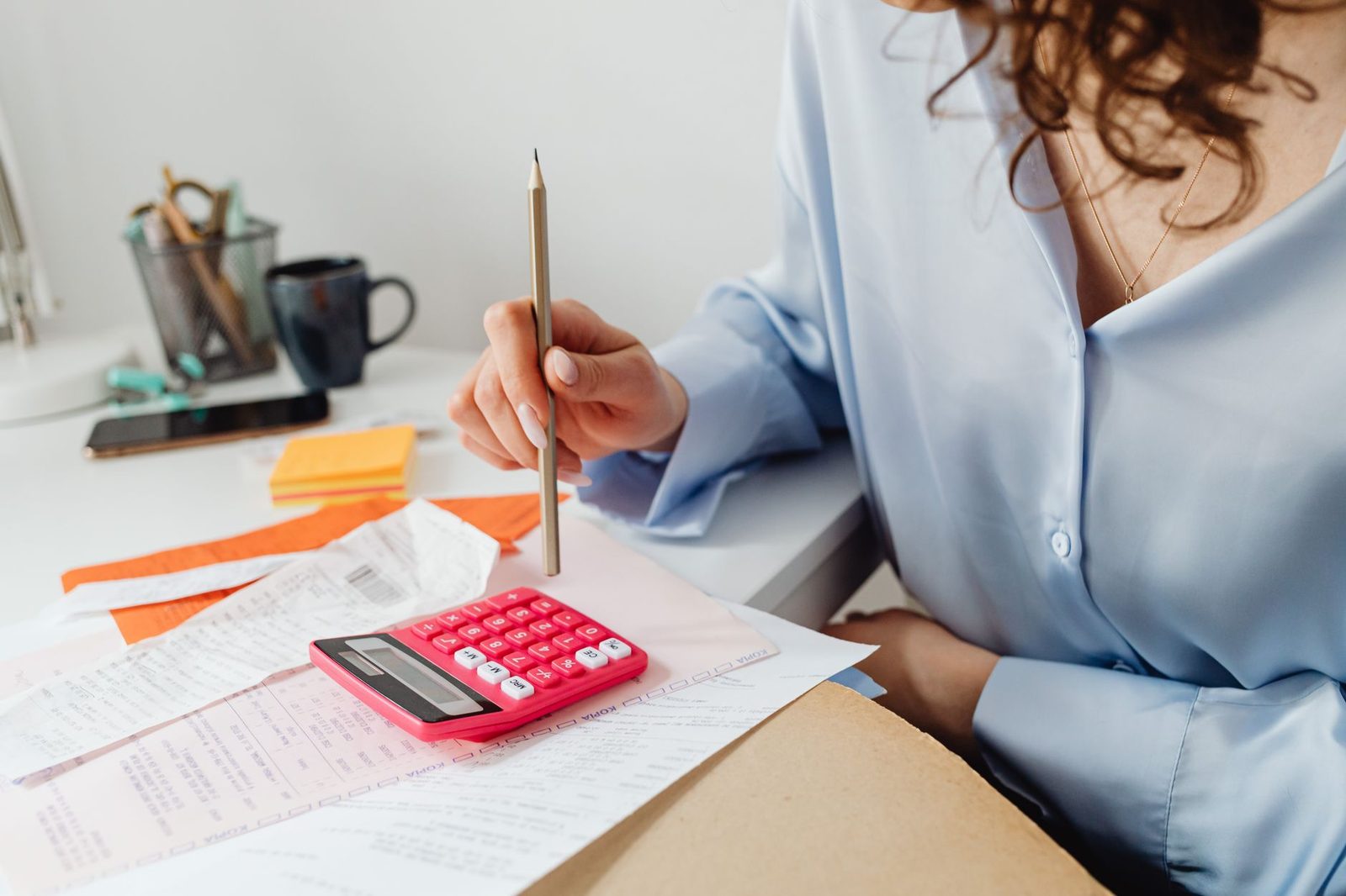 A person at a desk with a red calculator, notebook and printed pages