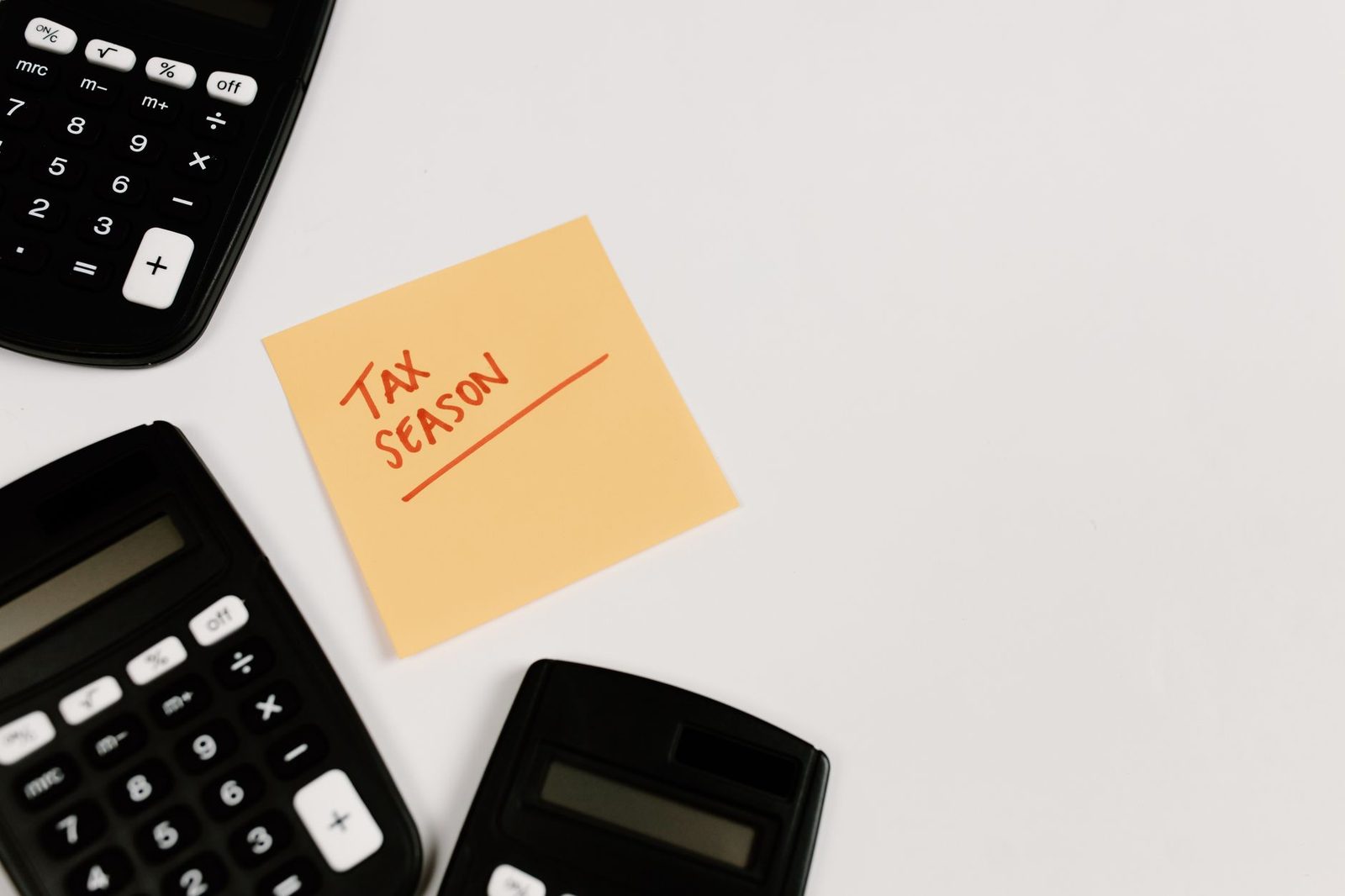 A sticky note reading tax season resting against a desktop calculator
