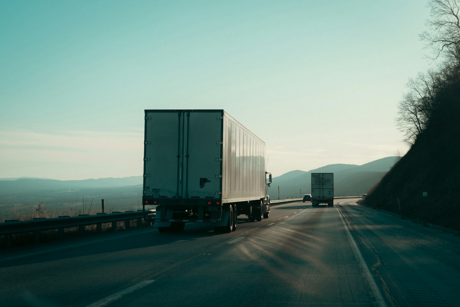 Two semi-trucks hauling freight on a highway, representing the trucking industry that drives the largest share of invoice factoring volume