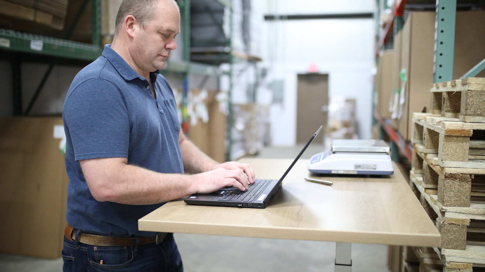 Small business owner in a warehouse reviewing accounts receivable and cash flow on a laptop