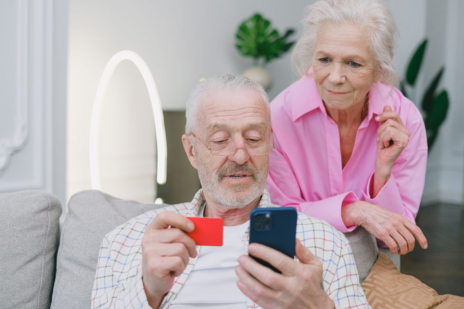 An older couple sitting together, one holding a phone and a card