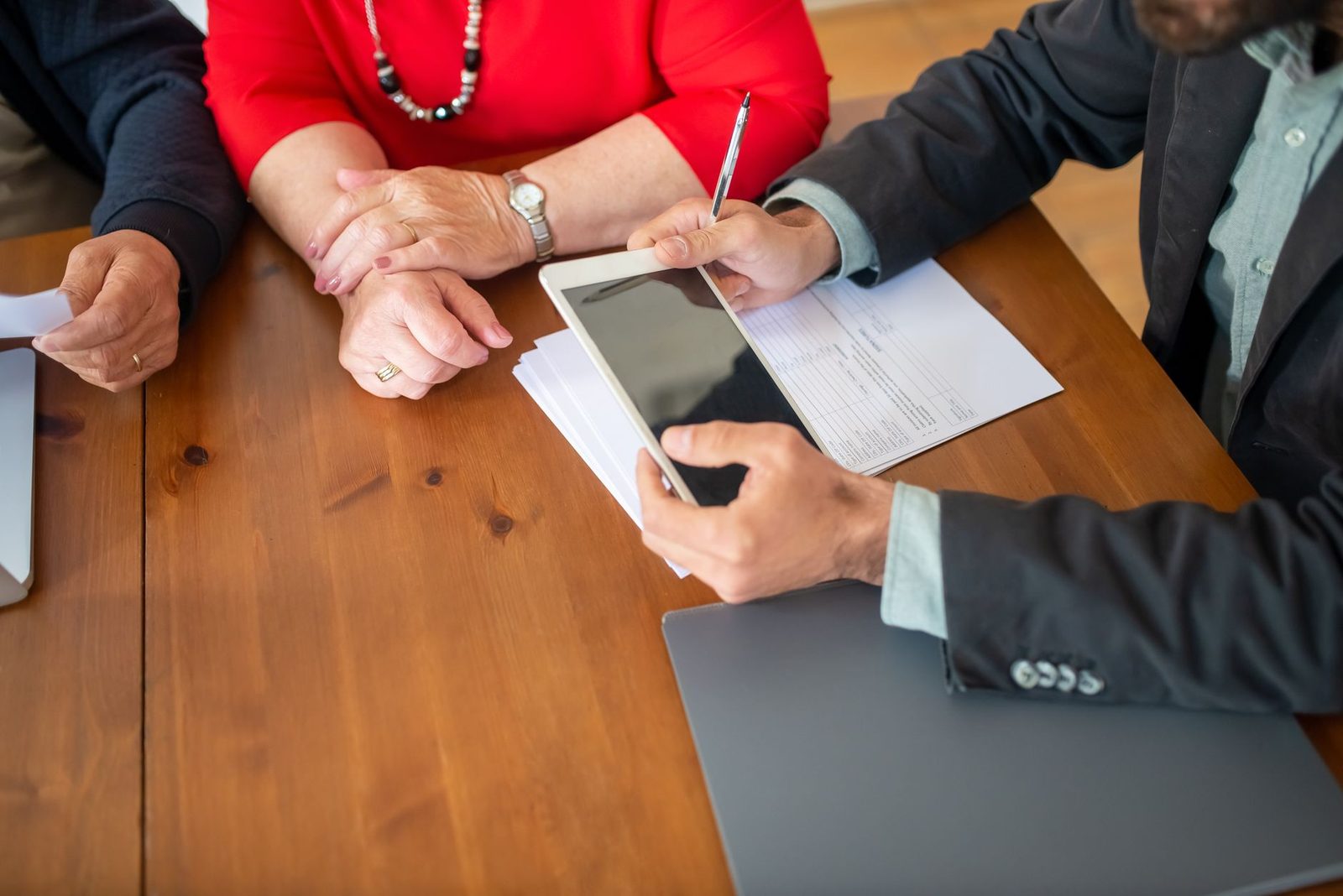 Hands around a table with a tablet, documents and a pen