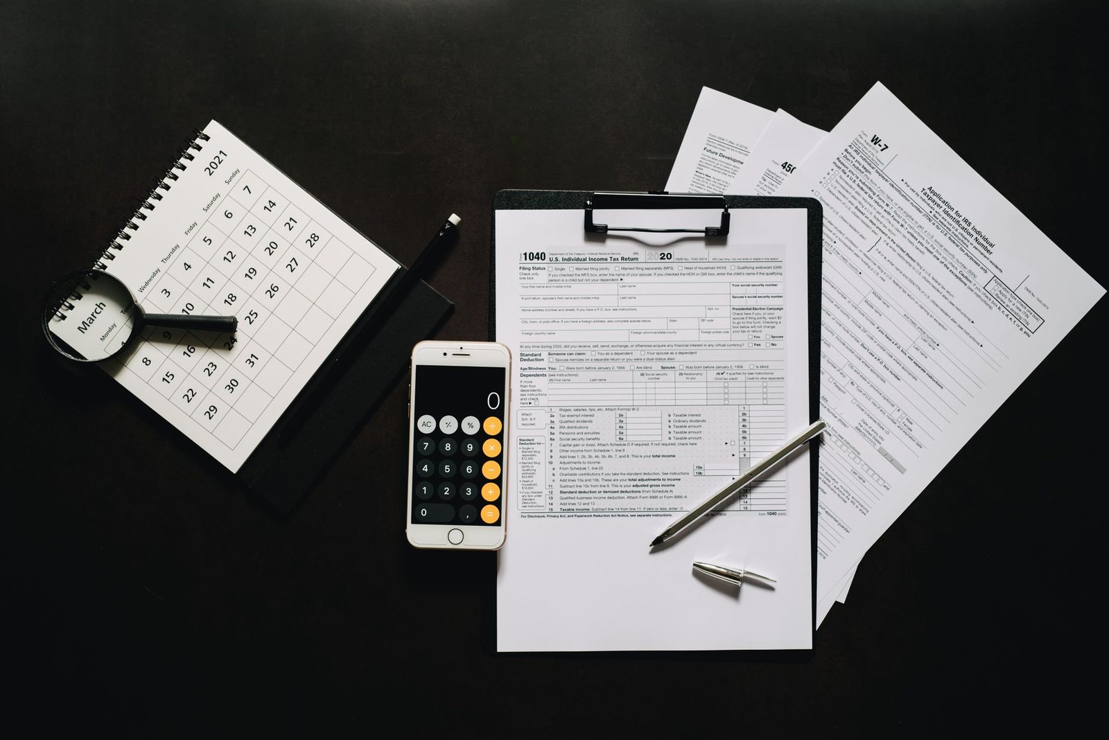 An overhead arrangement of tax forms, a calculator, a phone and a small calendar