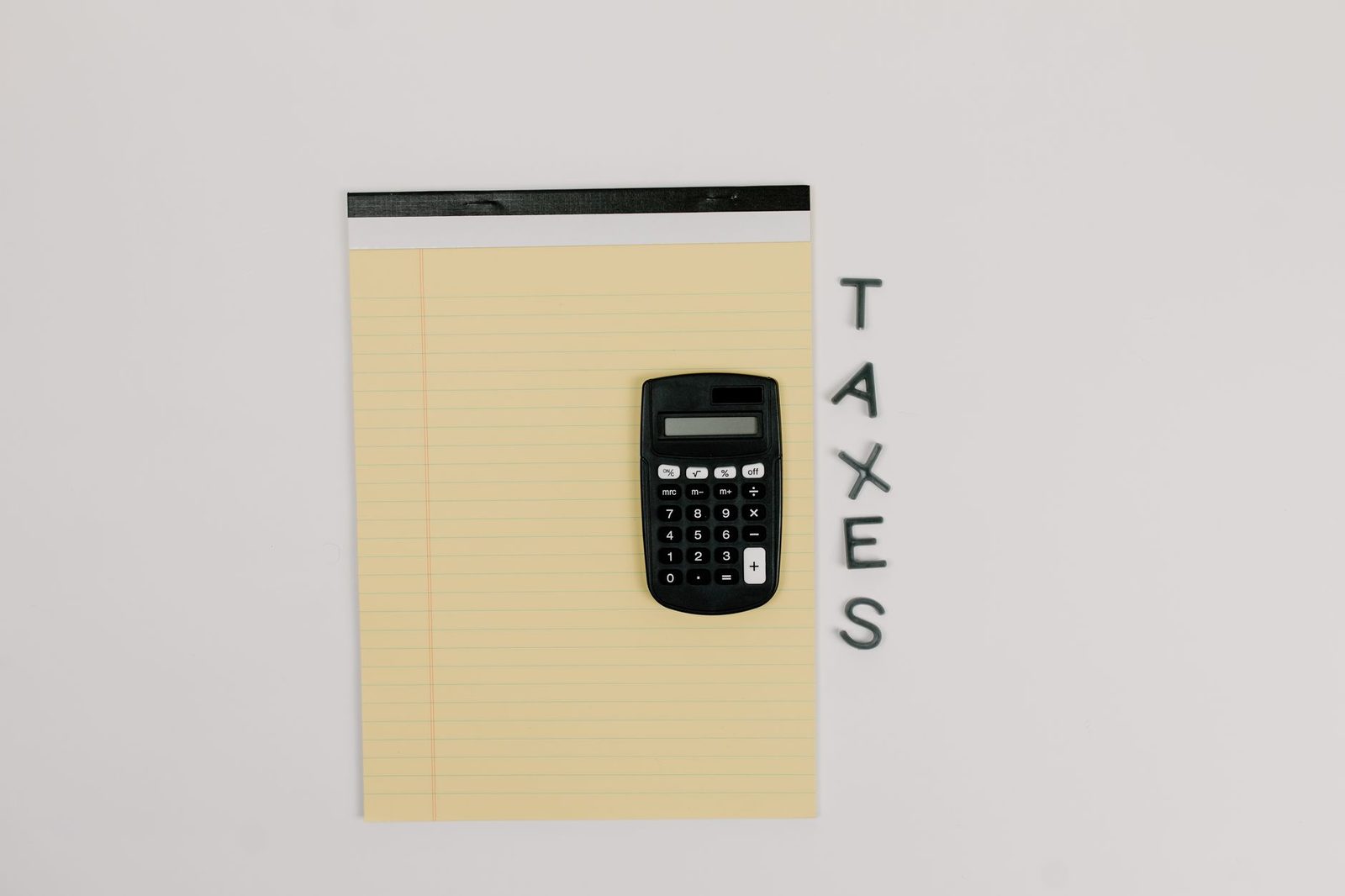 A yellow legal pad with the word taxes written down the margin and a calculator on top