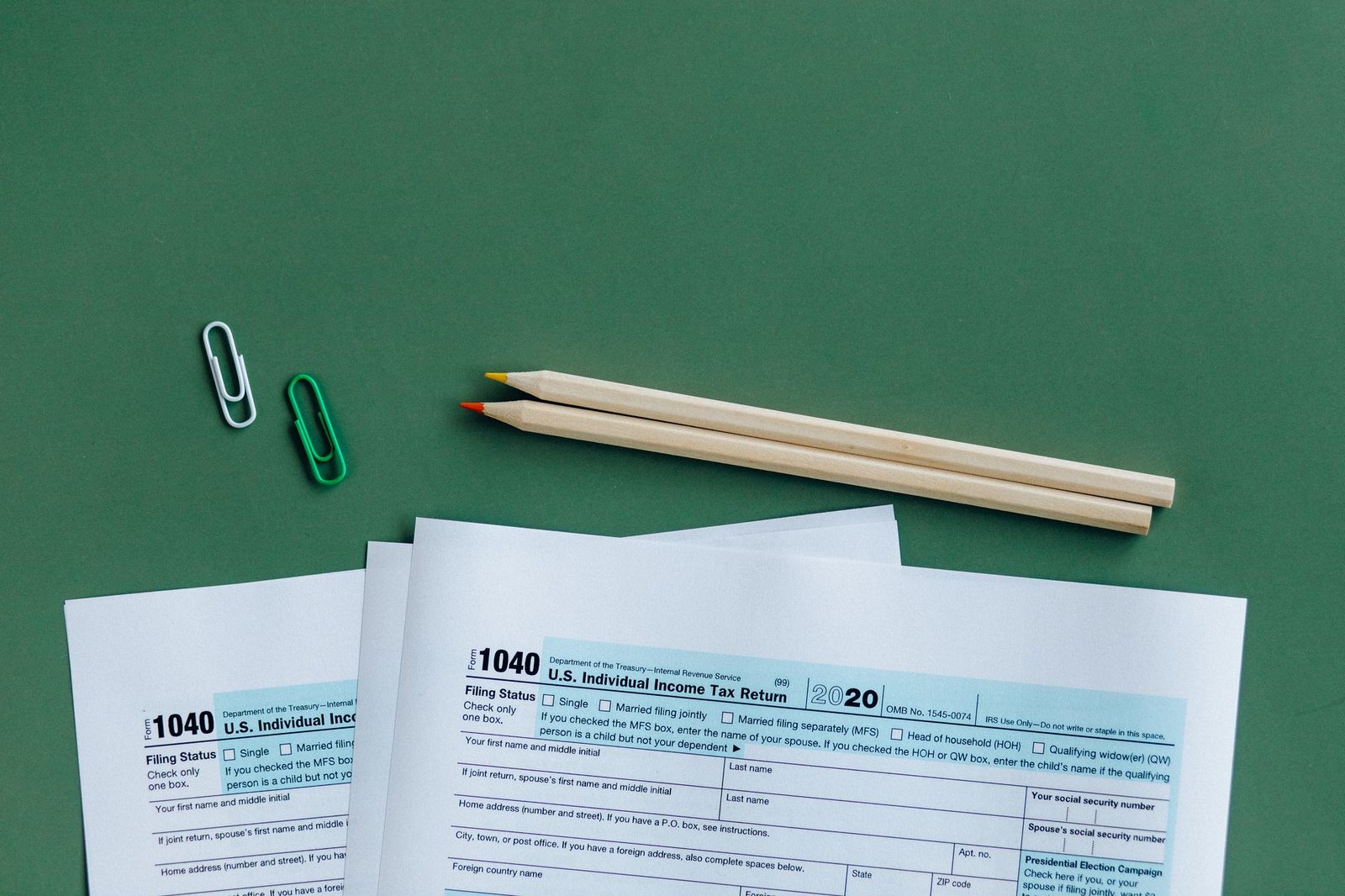 Two IRS Form 1040 tax returns lying on a green surface beside pencils