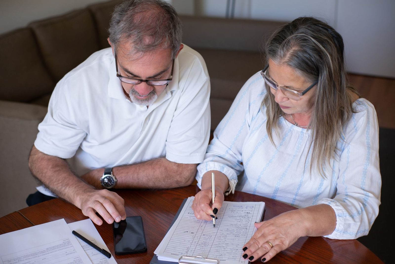 An older couple at a table working through paperwork together with a phone and pen