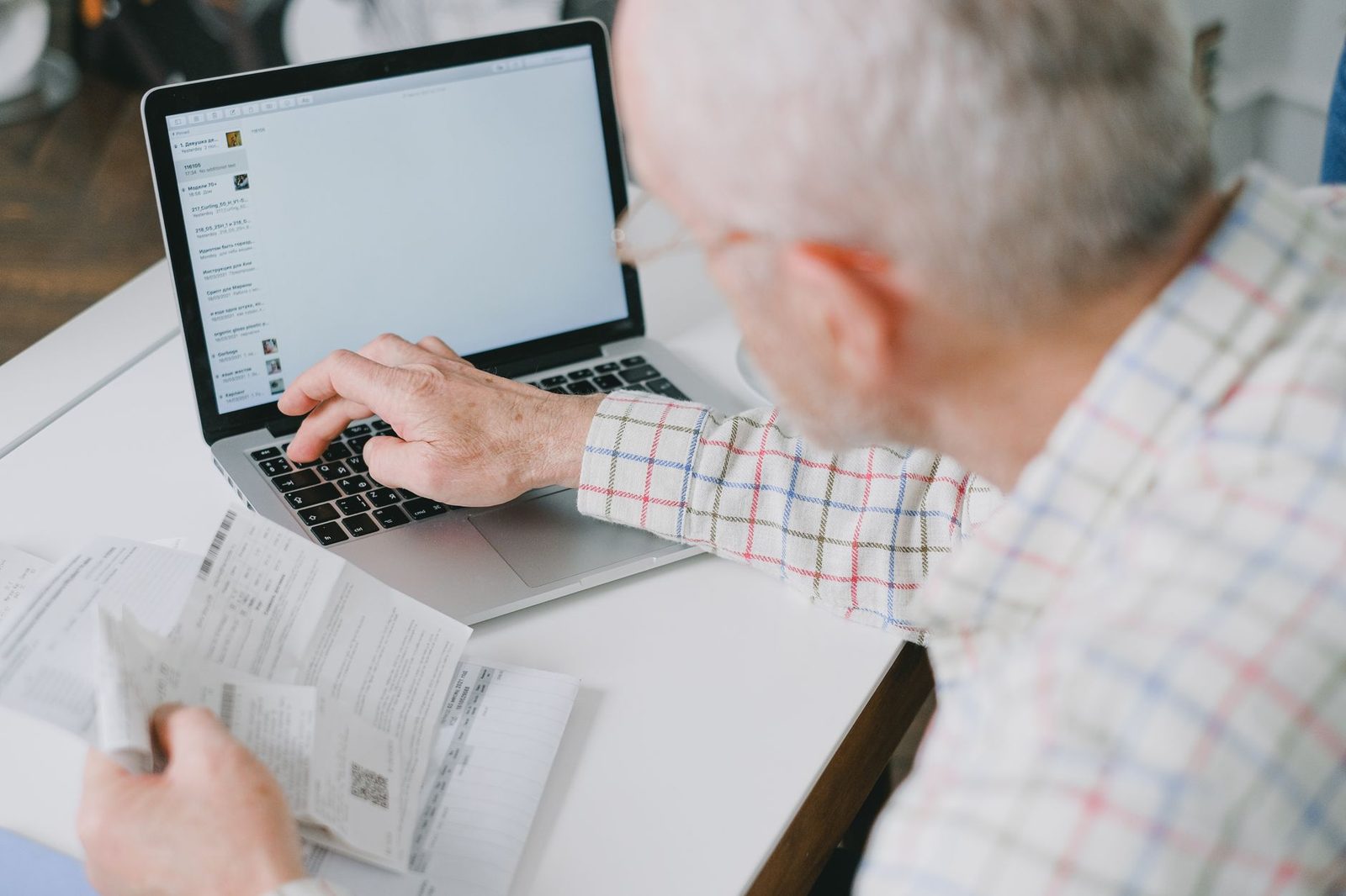 An older man working at a laptop with a calculator and printed documents