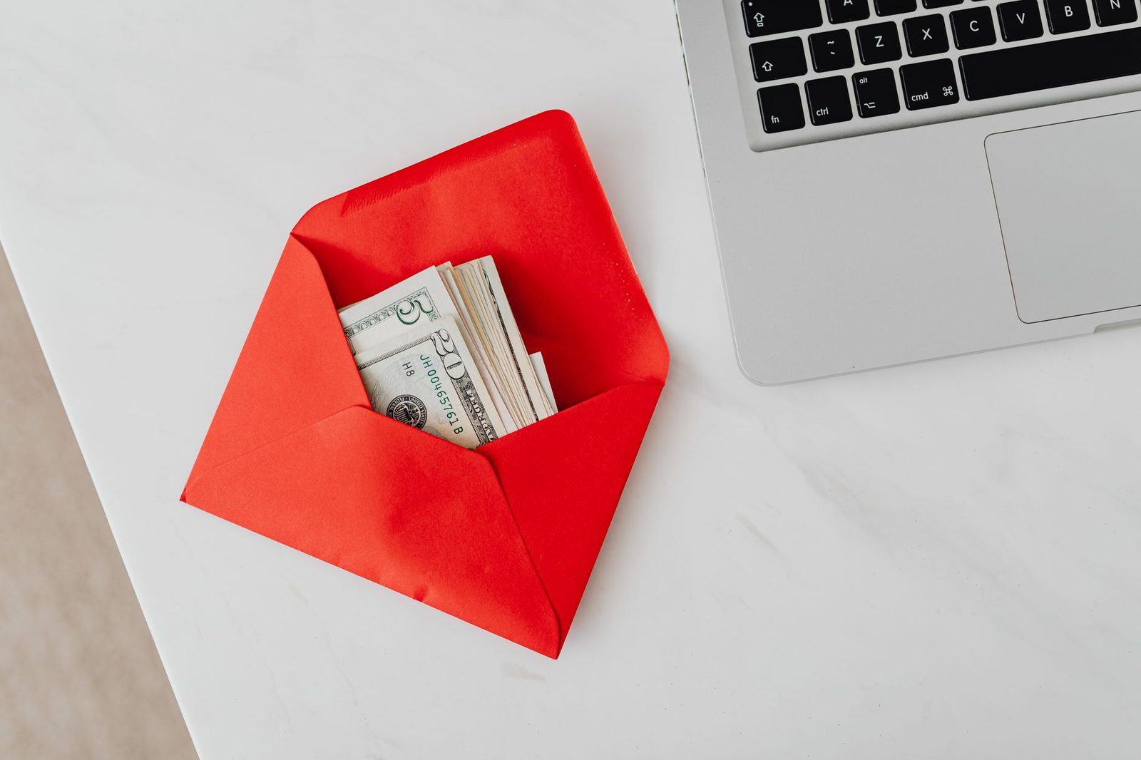 A red envelope with banknotes inside, sitting beside a laptop