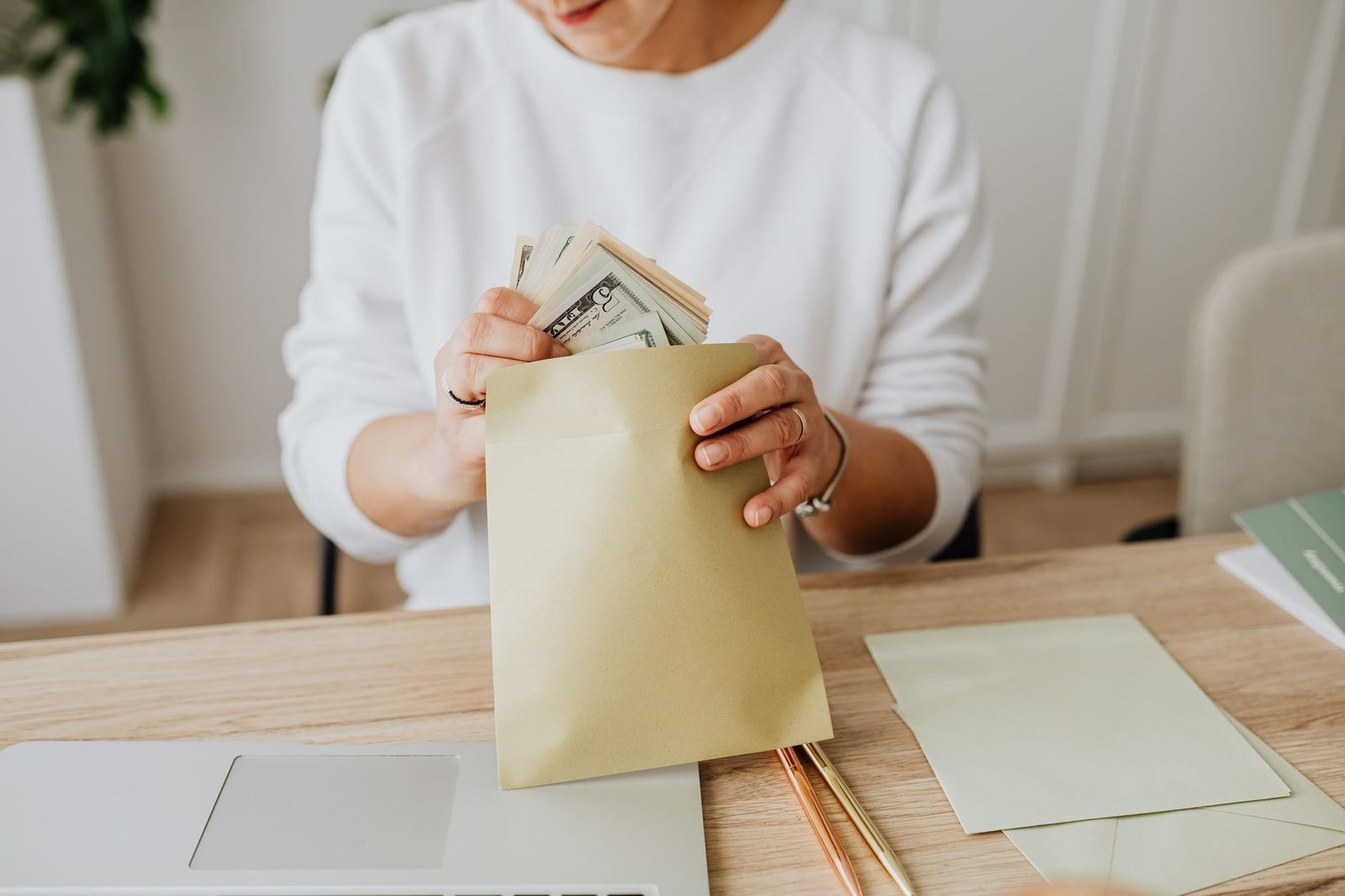 A person holding an open paper envelope at a desk with stationery