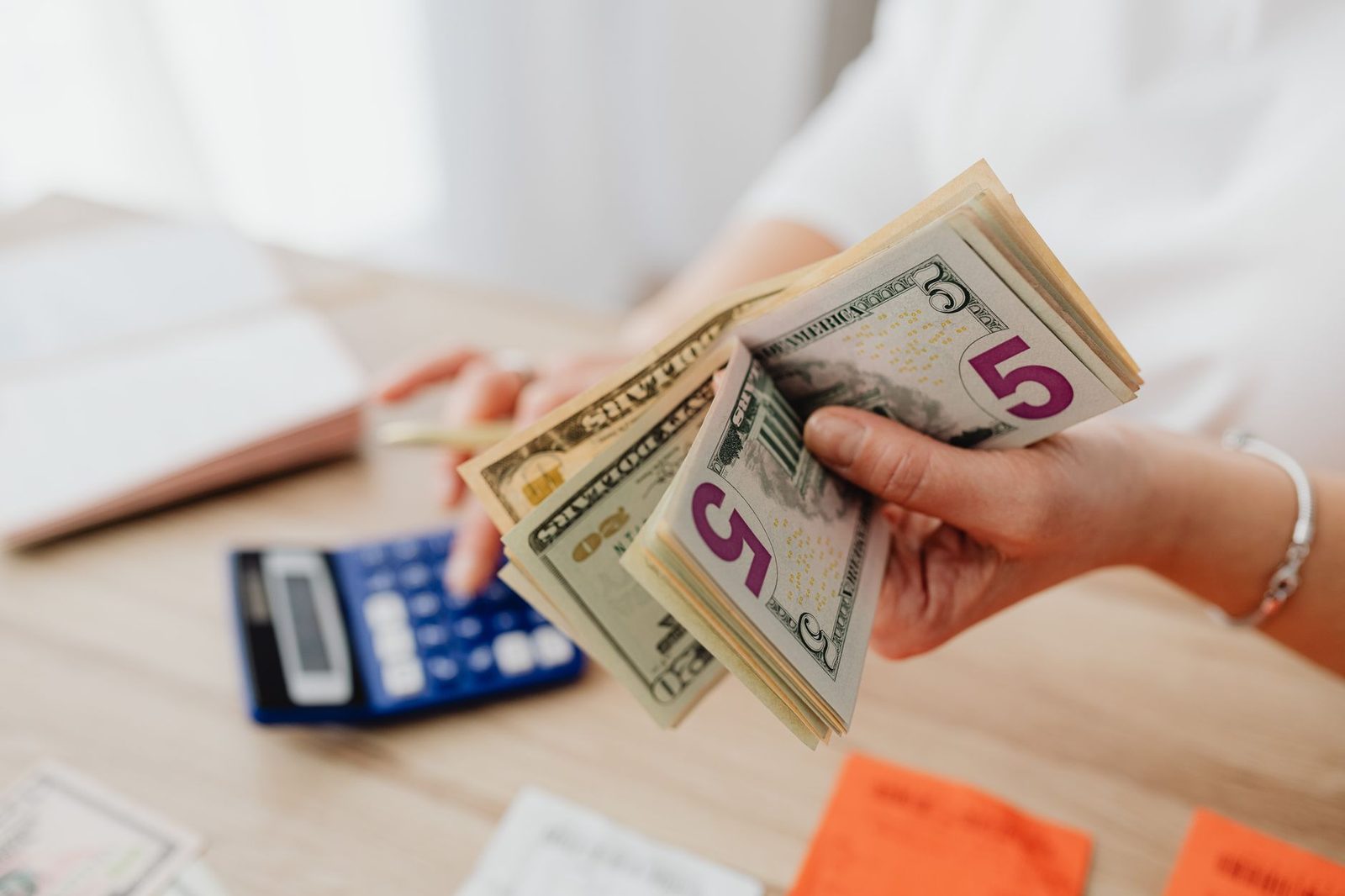 Hands counting banknotes beside a calculator and receipts on a desk