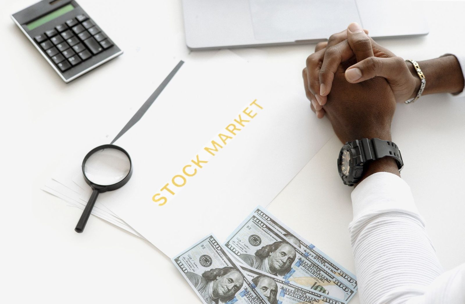 A desk with banknotes, a calculator and printed pages headed stock market